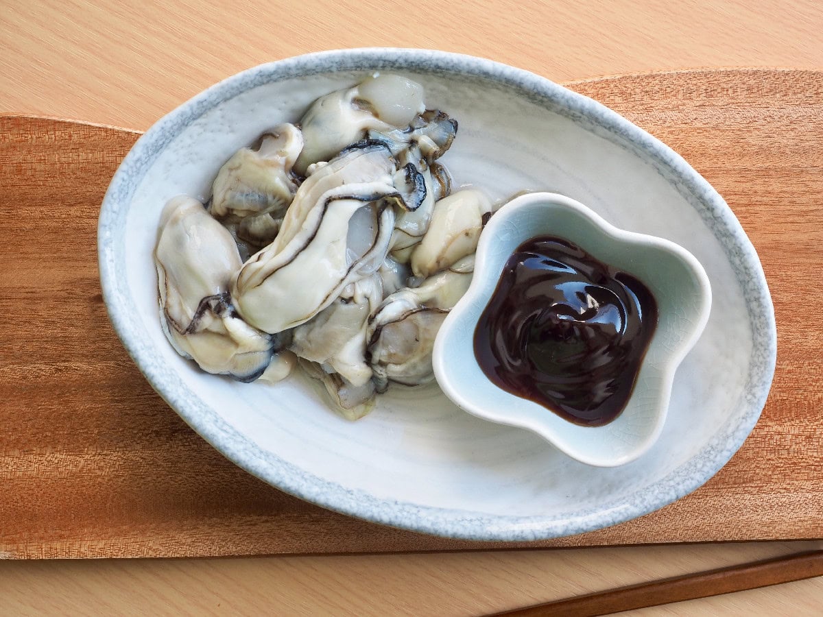 Raw oysters plated with a side of oyster sauce for serving.