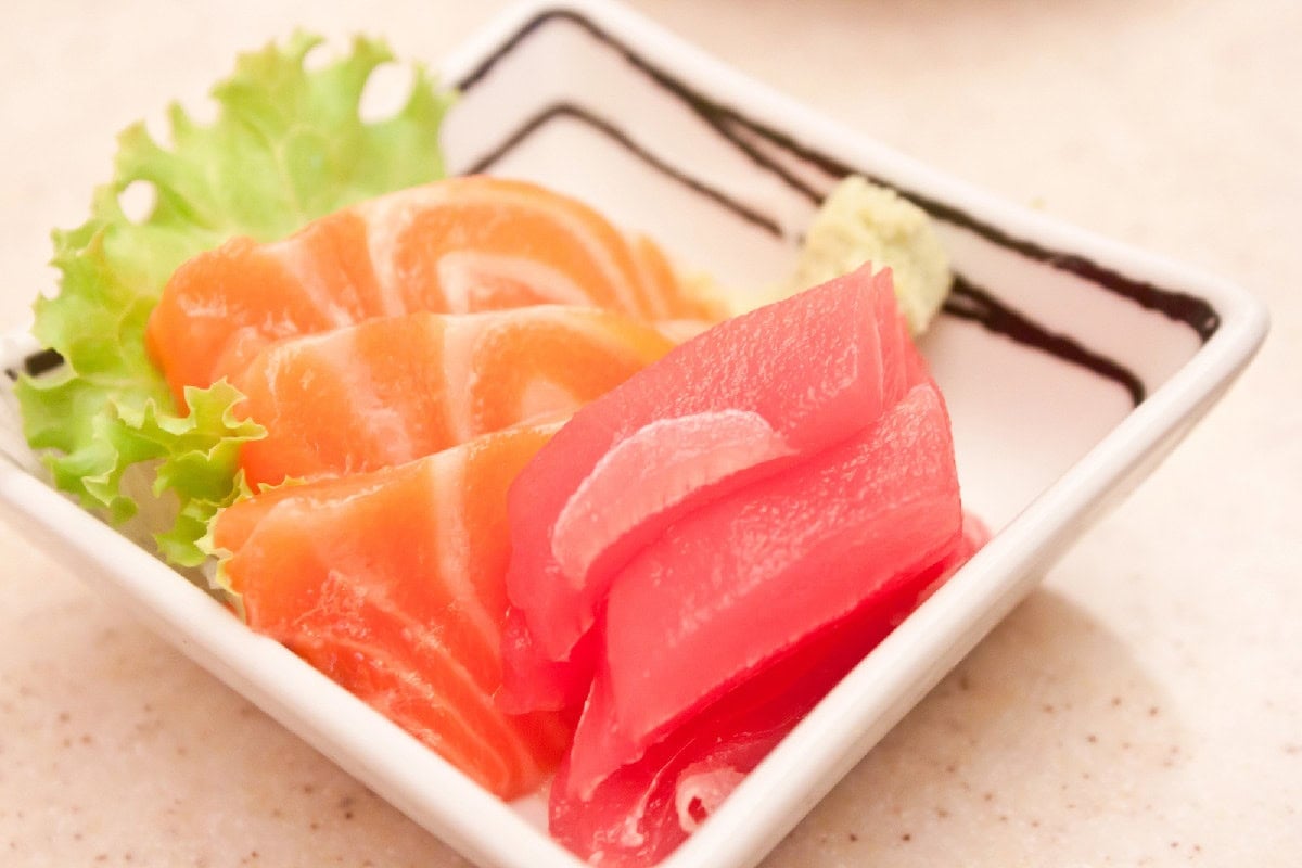 Salmon and tuna sashimi slices served on a white plate with lettuce, wasabi, and dipping sauce.