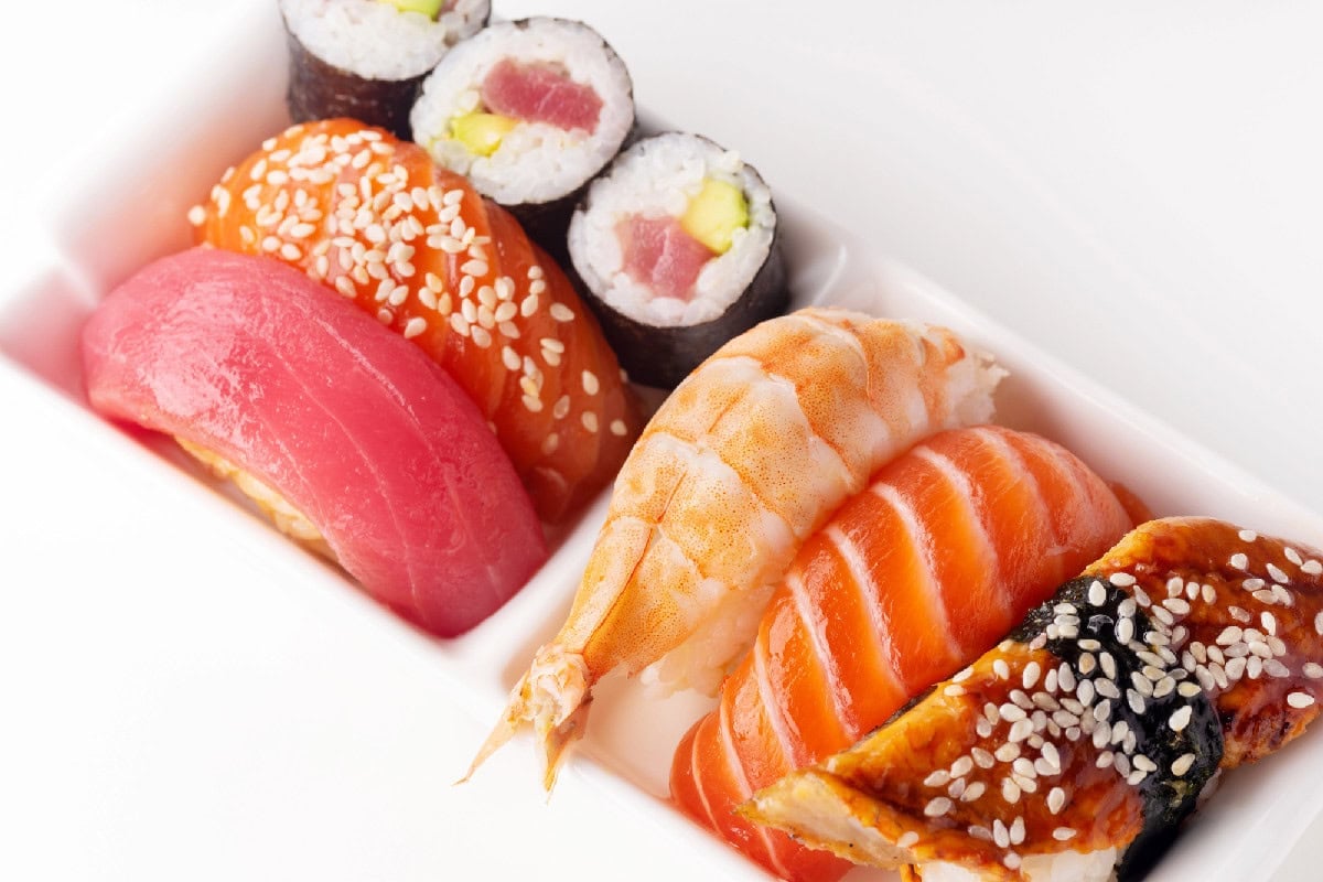 Assorted nigiri sushi including salmon, tuna, shrimp, and eel topped with sesame seeds on a white plate.