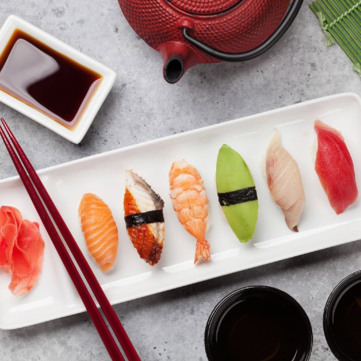 Nigiri sushi assortment with salmon, shrimp, eel, tuna, and avocado served alongside soy sauce and chopsticks.
