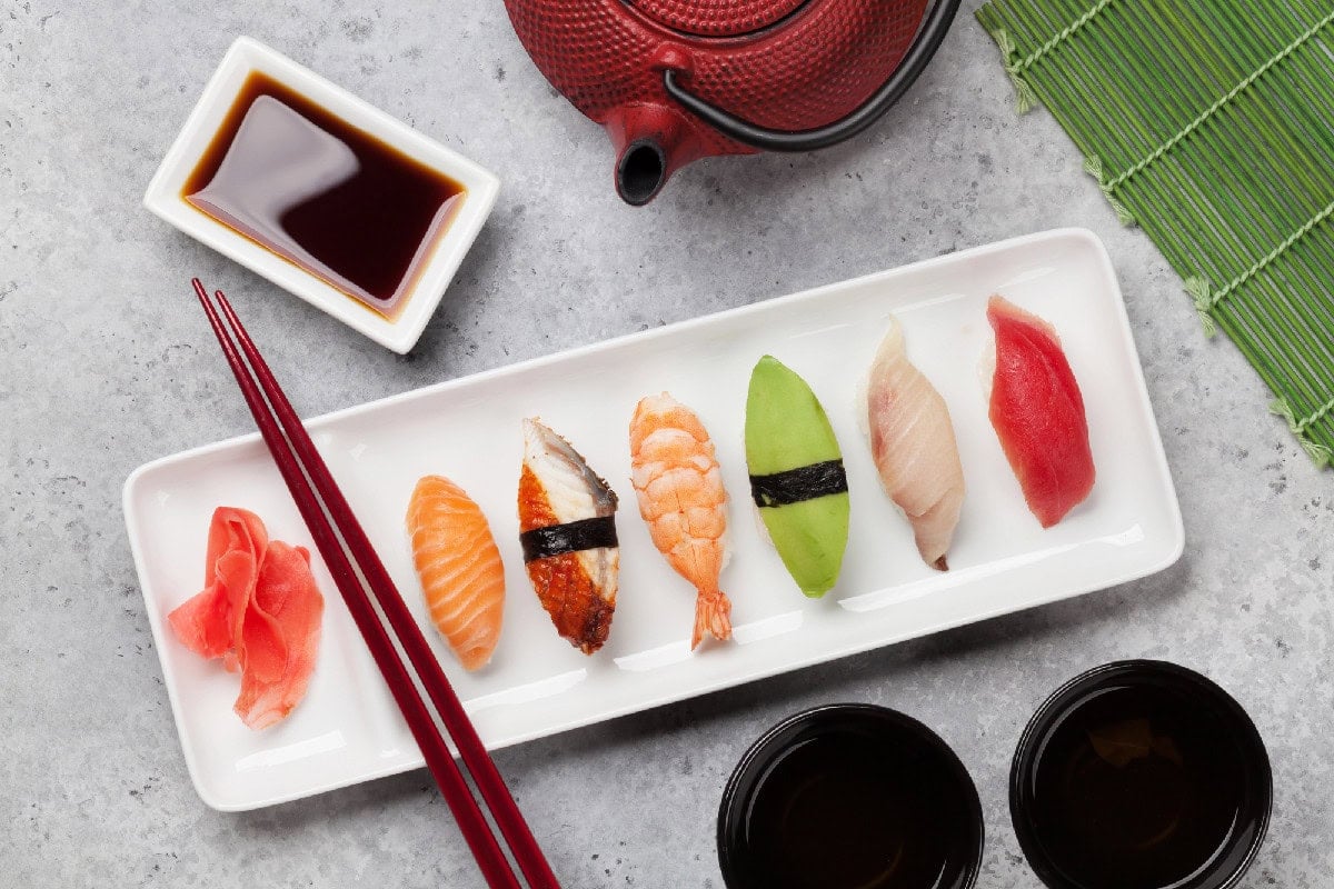 Nigiri sushi assortment with salmon, shrimp, eel, tuna, and avocado served alongside light soy sauce and chopsticks.