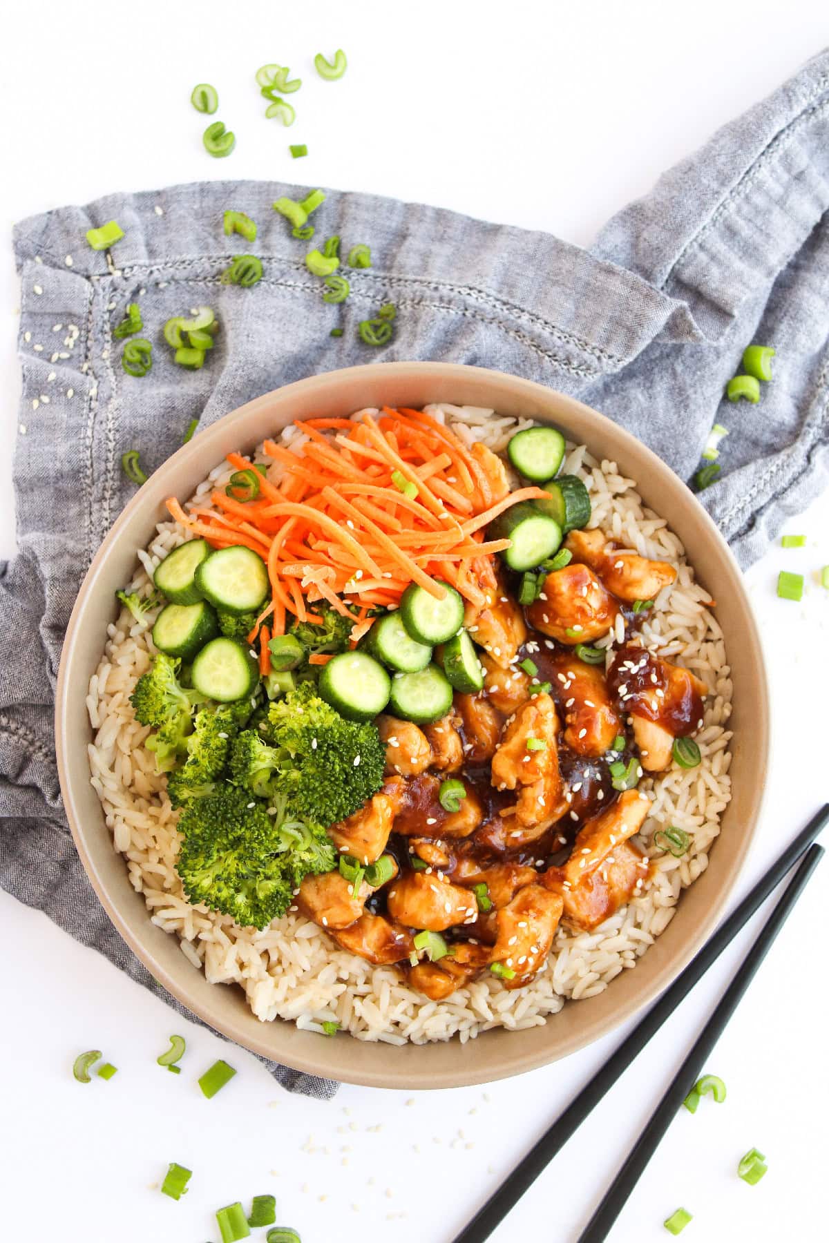 Teriyaki chicken rice bowl with broccoli, cucumber slices, shredded carrots, and sesame seeds.
