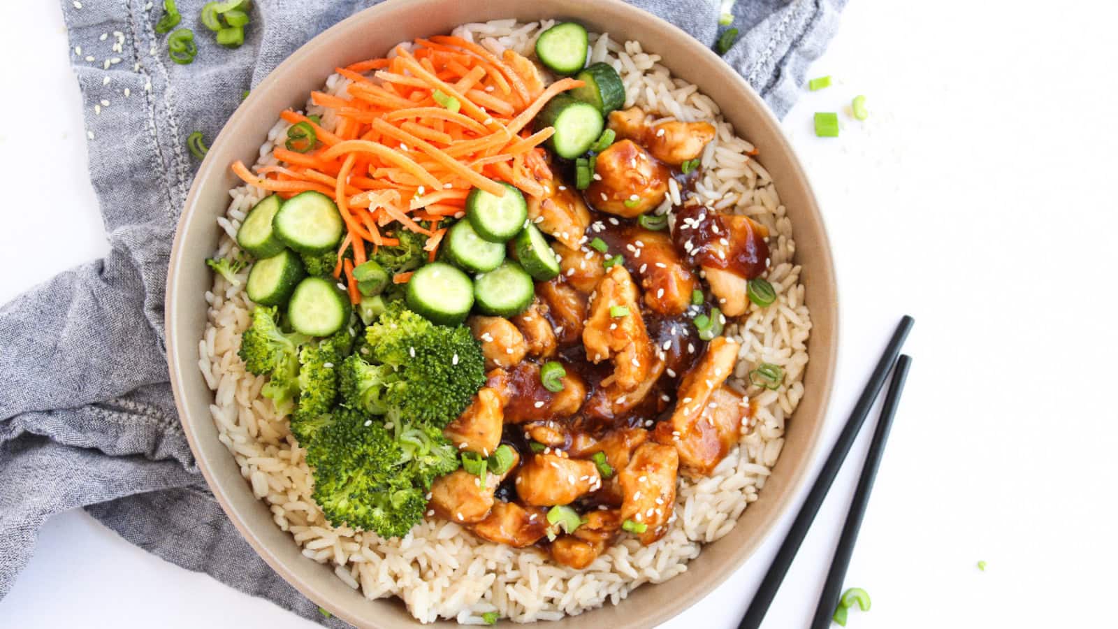 Teriyaki chicken rice bowl with glossy sauce, green onions, and fresh vegetables.