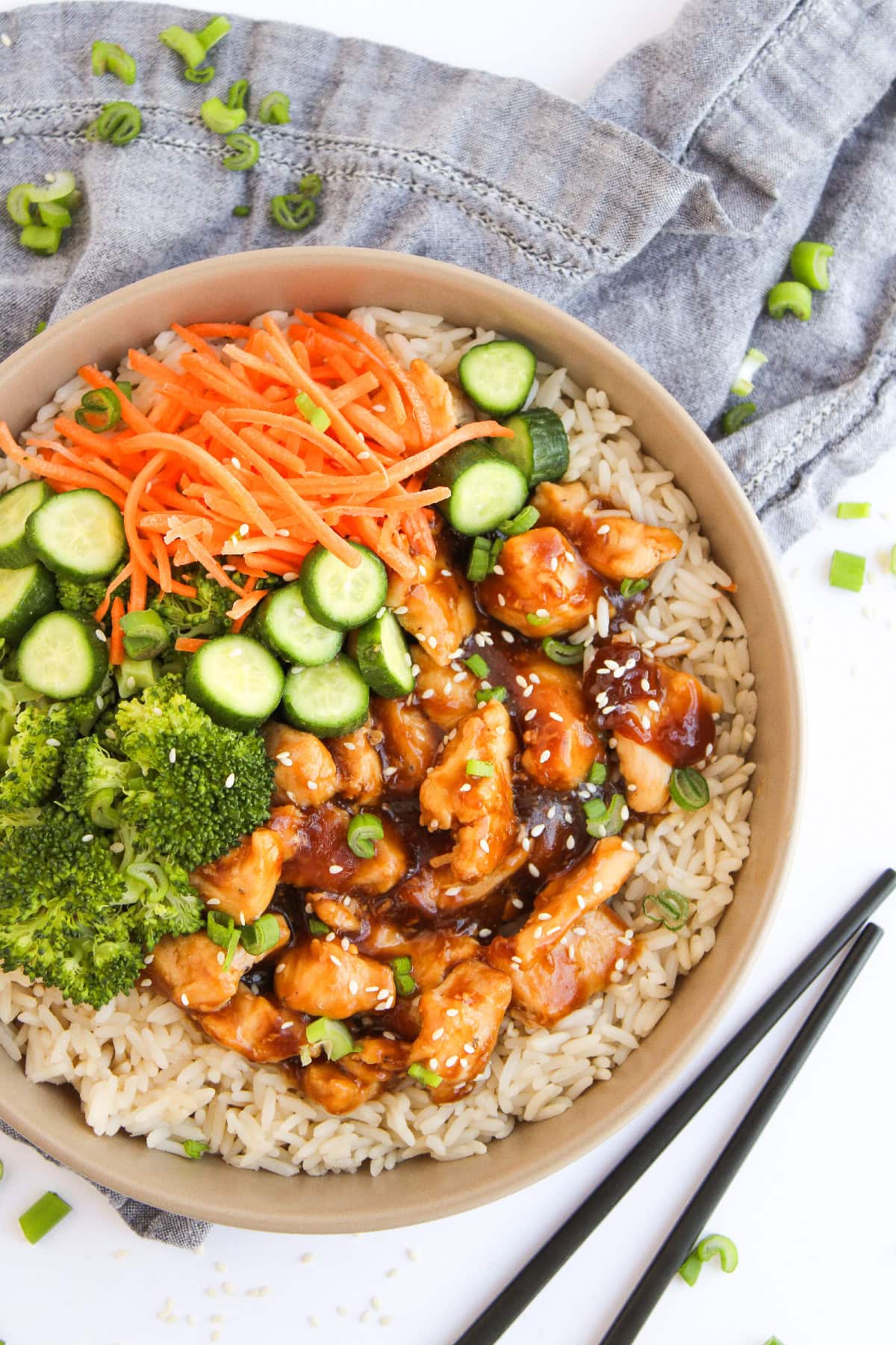 Teriyaki chicken bowl with steamed rice, broccoli, cucumbers, carrots, and glossy sauce.