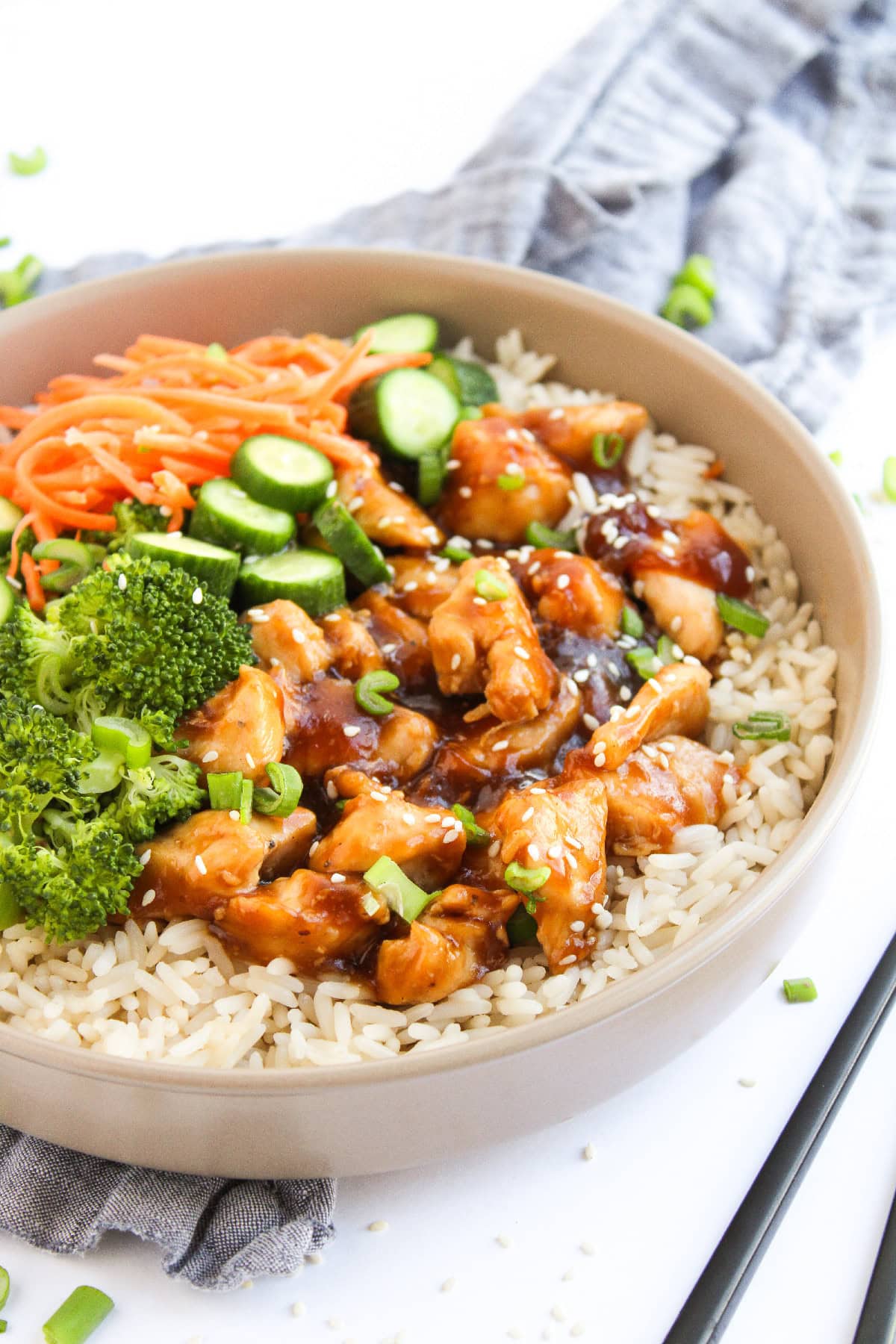 Teriyaki chicken served over rice with fresh vegetables in a bowl, side angle view.