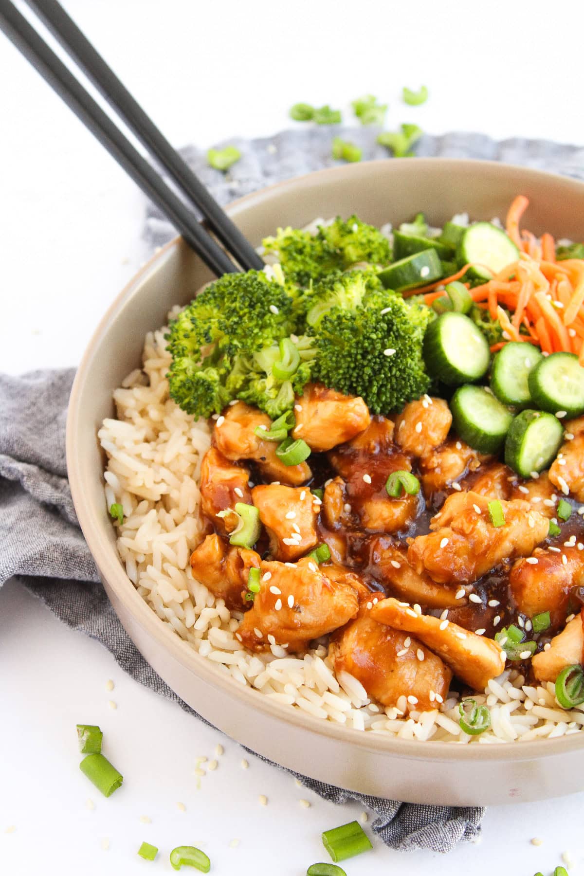 Teriyaki chicken rice bowl with broccoli and chopsticks, garnished with sesame seeds.