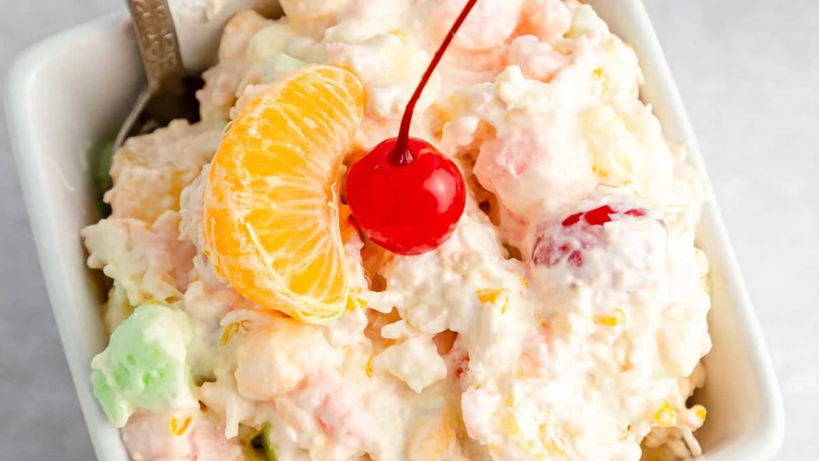 Ambrosia salad mixed with fruit, marshmallows, and creamy dressing.