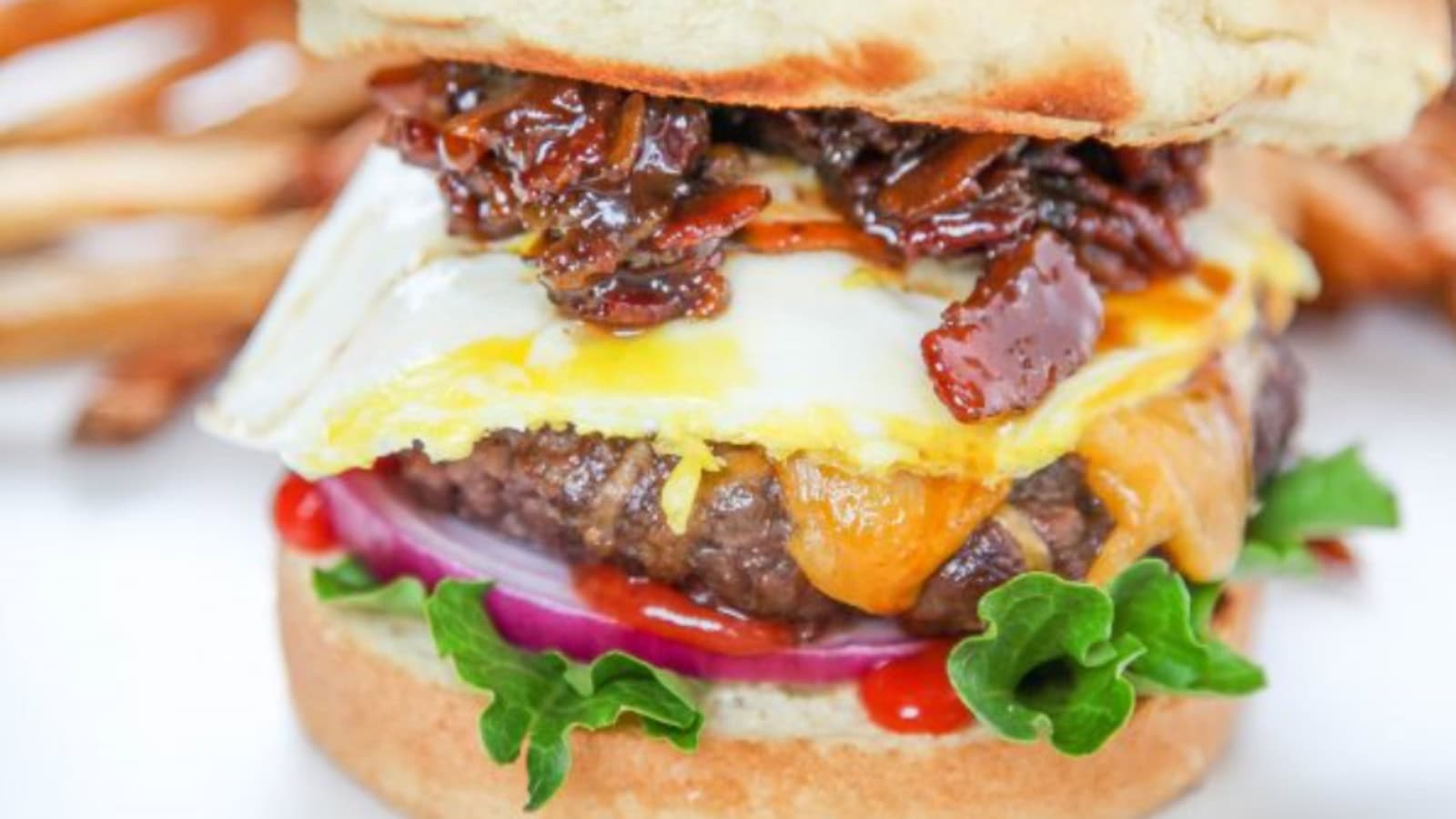 Breakfast burger stacked with egg, cheese, and savory meat on a bun.