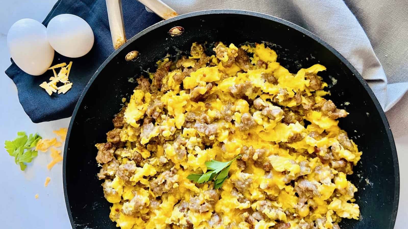 Egg scramble mixed with sausage and melted cheese in a skillet.