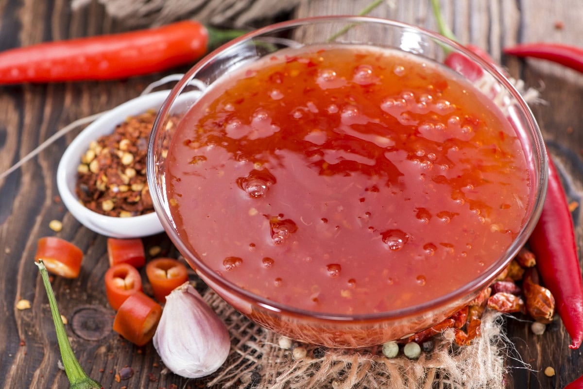 Bowl of chili garlic sauce surrounded by fresh red chilies, garlic, and chili flakes.