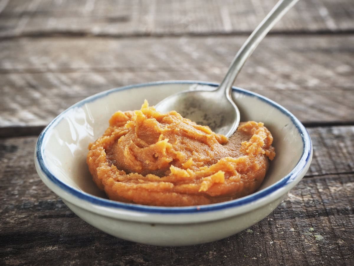 Miso paste in a ceramic bowl with a spoon on a rustic wooden surface.