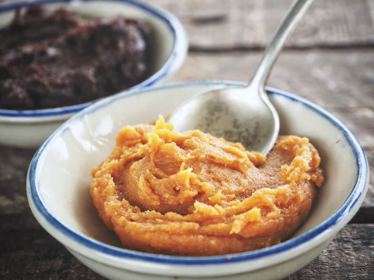 Close-up of miso paste in a bowl with spoon and fermented paste in the background.