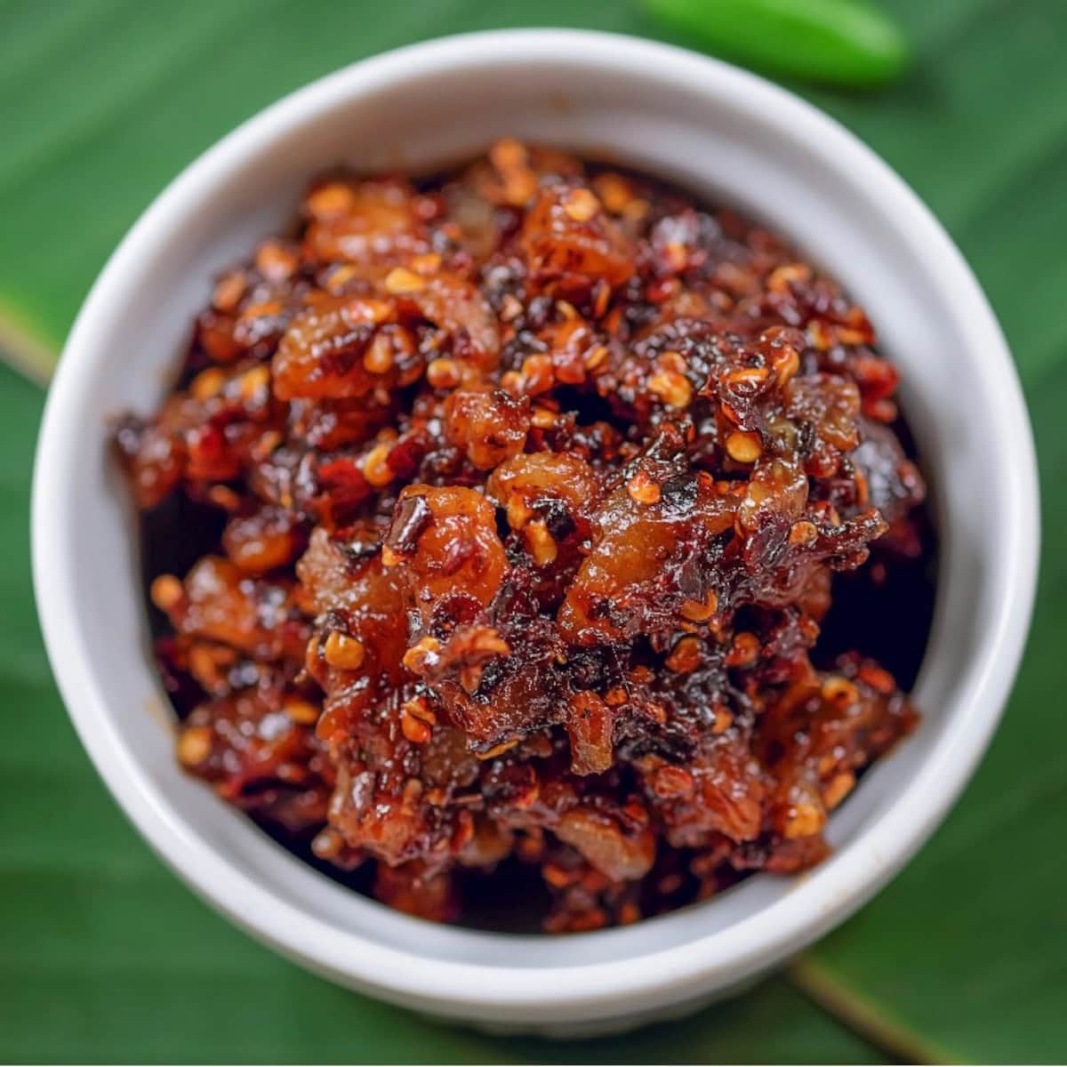 Close-up of Thai chili paste in a white bowl on a green leaf background.