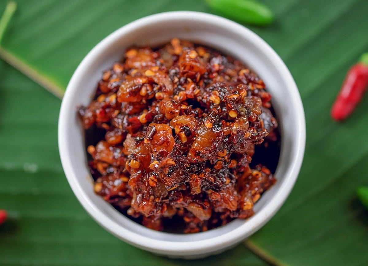 Thai chili paste in a white bowl with green leaves and red chilies.