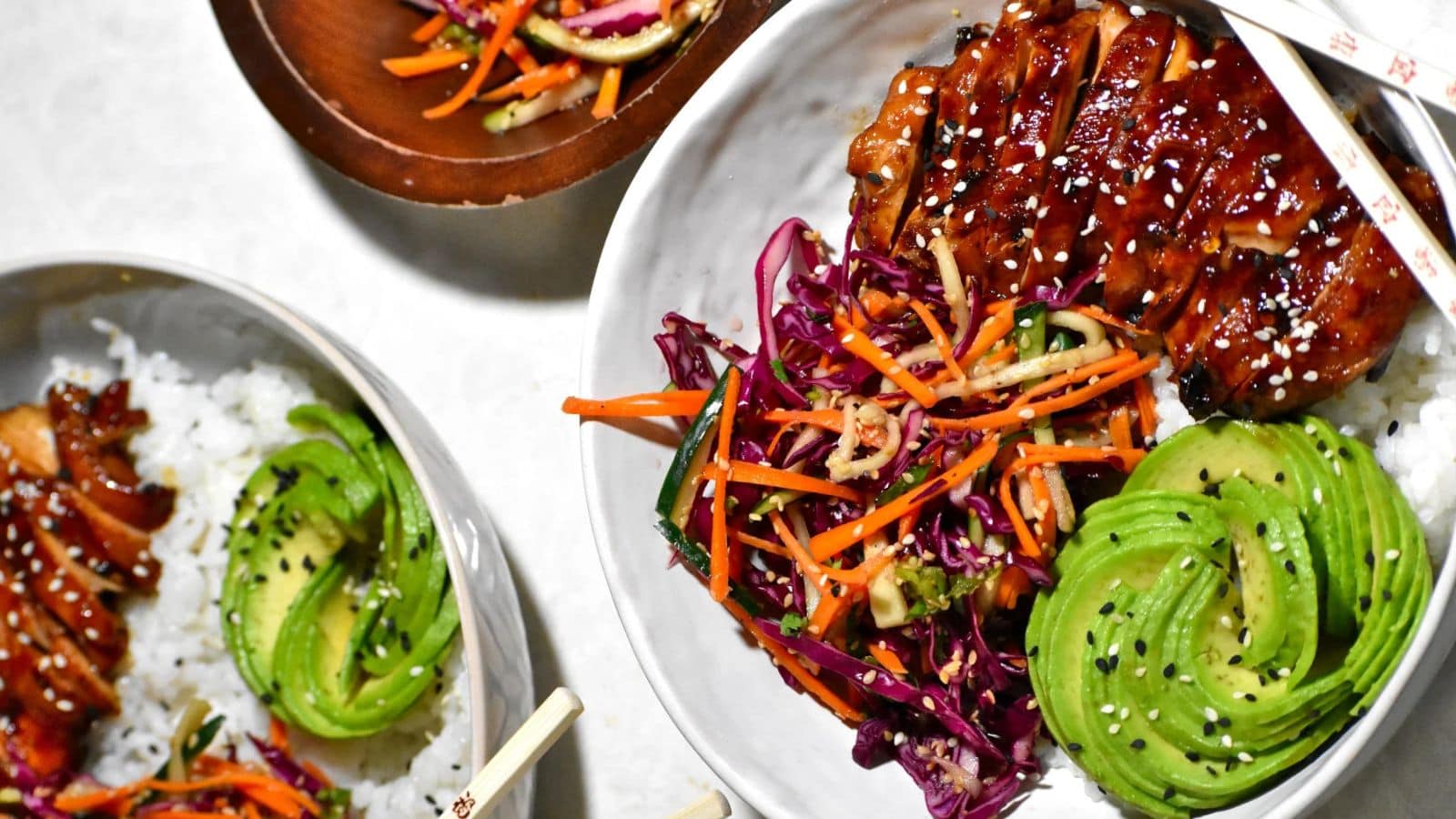 Fresh Asian dishes with rice, vegetables, and glazed meat on white plates.