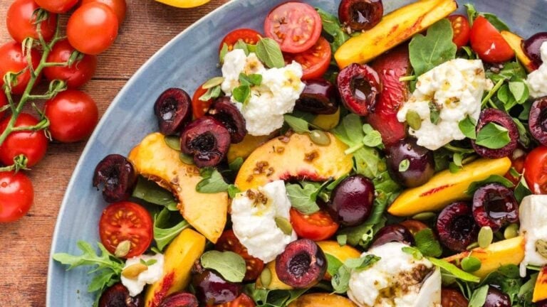 Peach salad topped with creamy burrata and fresh greens.