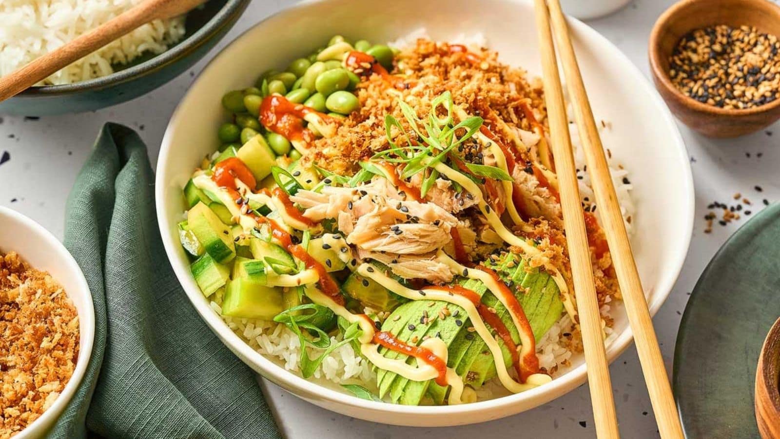 Spicy tuna rice bowl topped with avocado, sauce, and fresh garnishes.