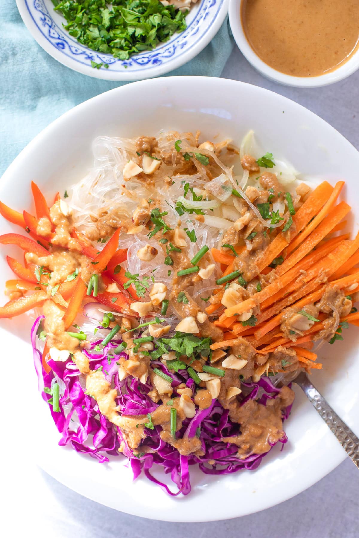 Close-up spring roll noodle bowl topped with crunchy vegetables, chopped peanuts, fresh herbs, and peanut dressing.