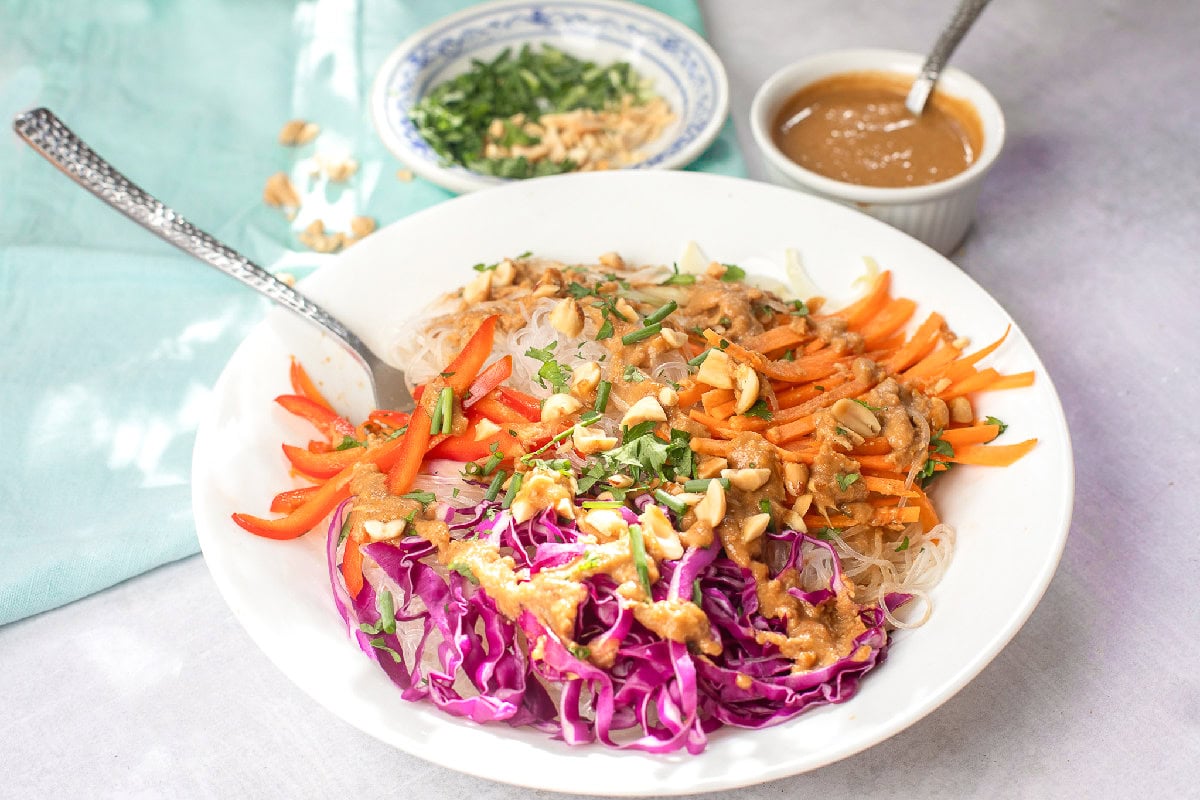 Fresh spring roll bowl with rice noodles, crunchy vegetables, and creamy peanut dressing on a white plate.