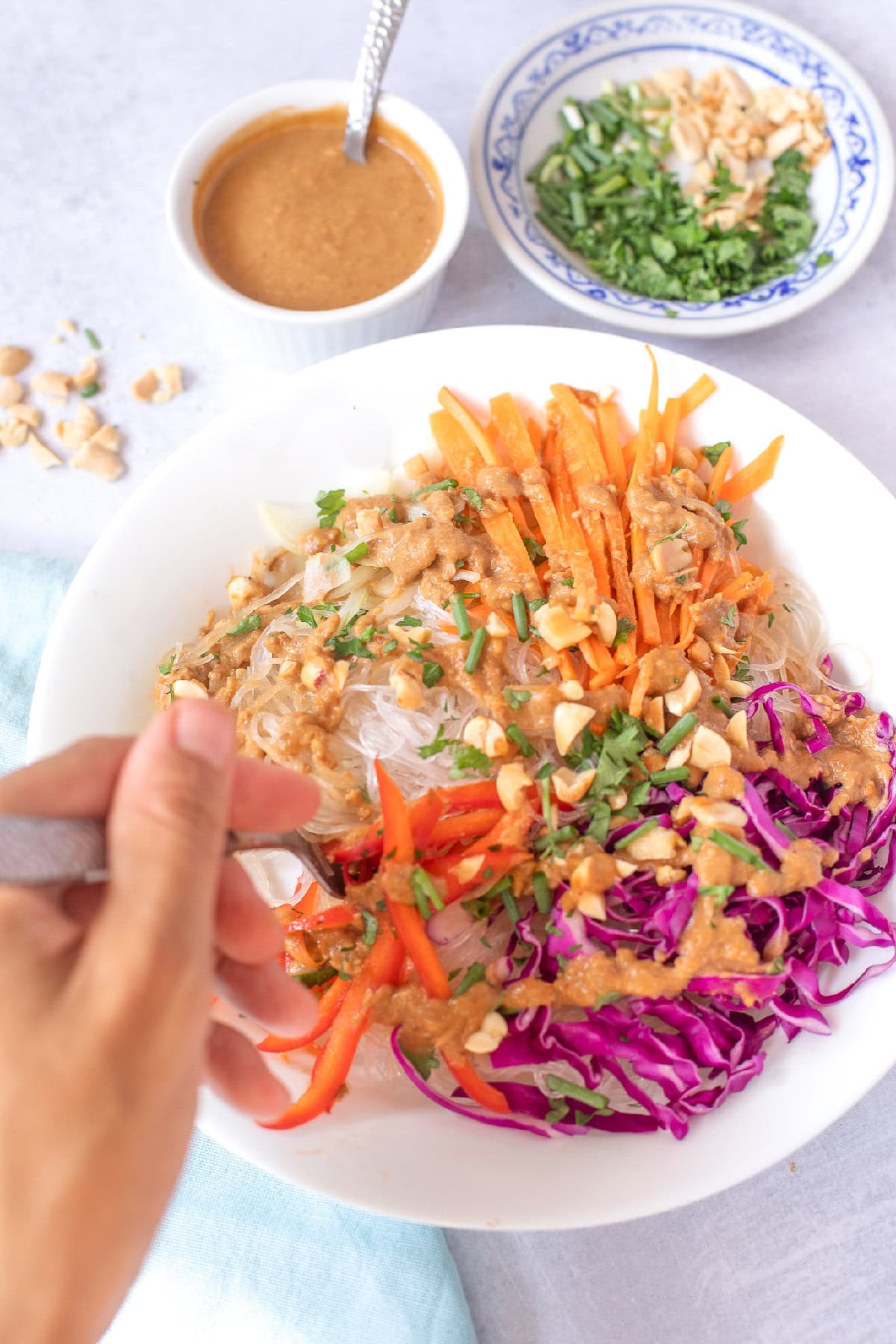 Spring roll in a bowl with rice noodles, fresh vegetables, peanut sauce, and chopped peanuts.