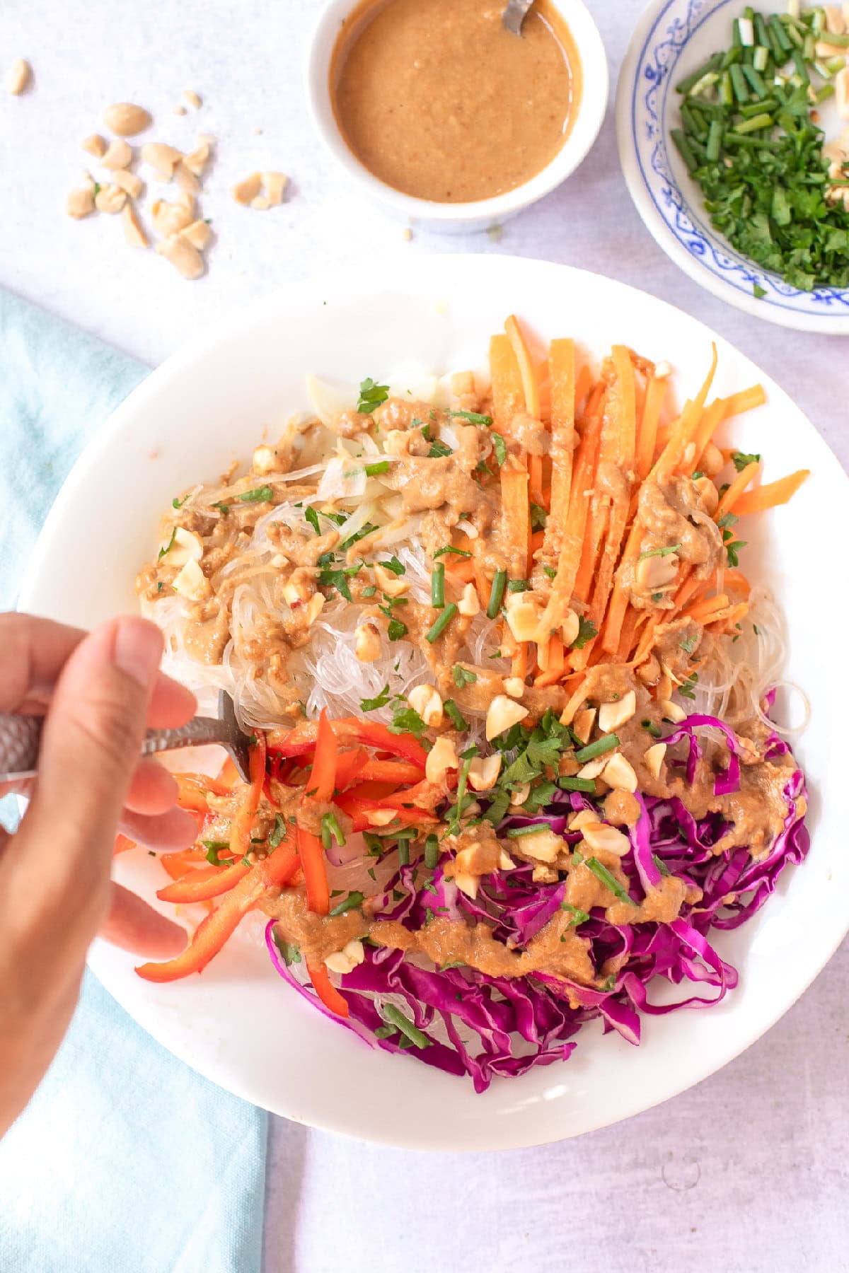 Hand holding a fork over a fresh spring roll bowl with rice noodles, vegetables, herbs, and creamy peanut dressing.