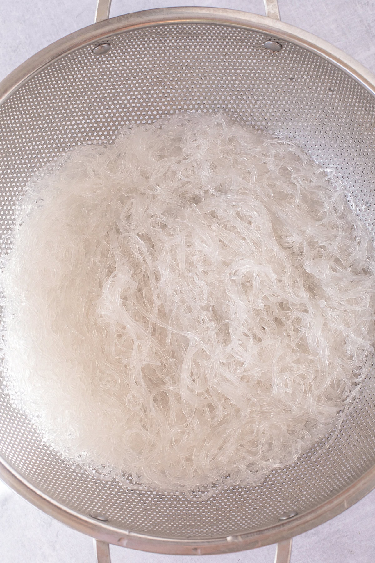 Cooked rice noodles draining in a metal colander for spring roll in a bowl recipe.