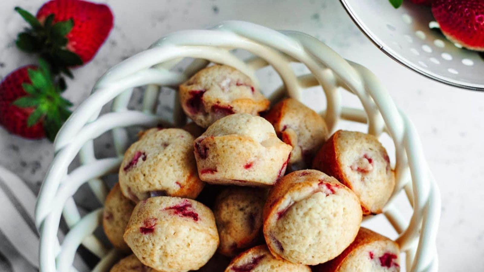 Mini strawberry muffins baked fluffy with fresh berry pieces throughout.