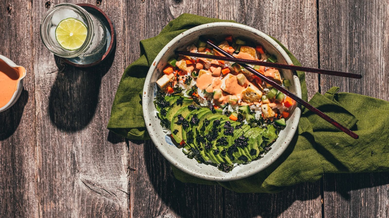 Sushi bowl filled with vegetables, rice, and drizzled spicy mayo.