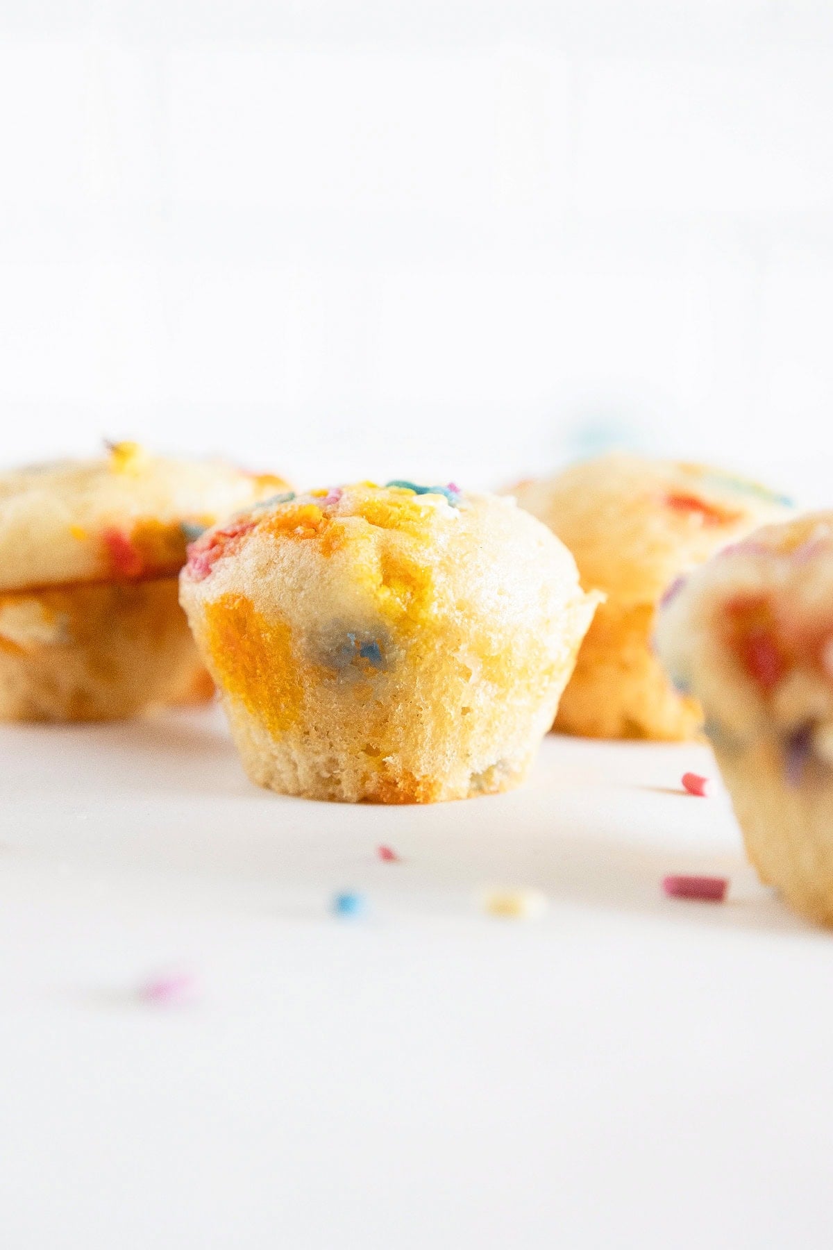 Birthday cake mini muffin with colorful sprinkles and blurred muffins in the background.