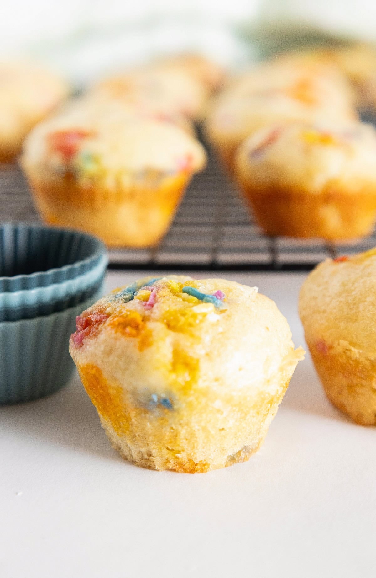 Birthday cake mini muffin with colorful sprinkles beside silicone muffin liners on a white surface.
