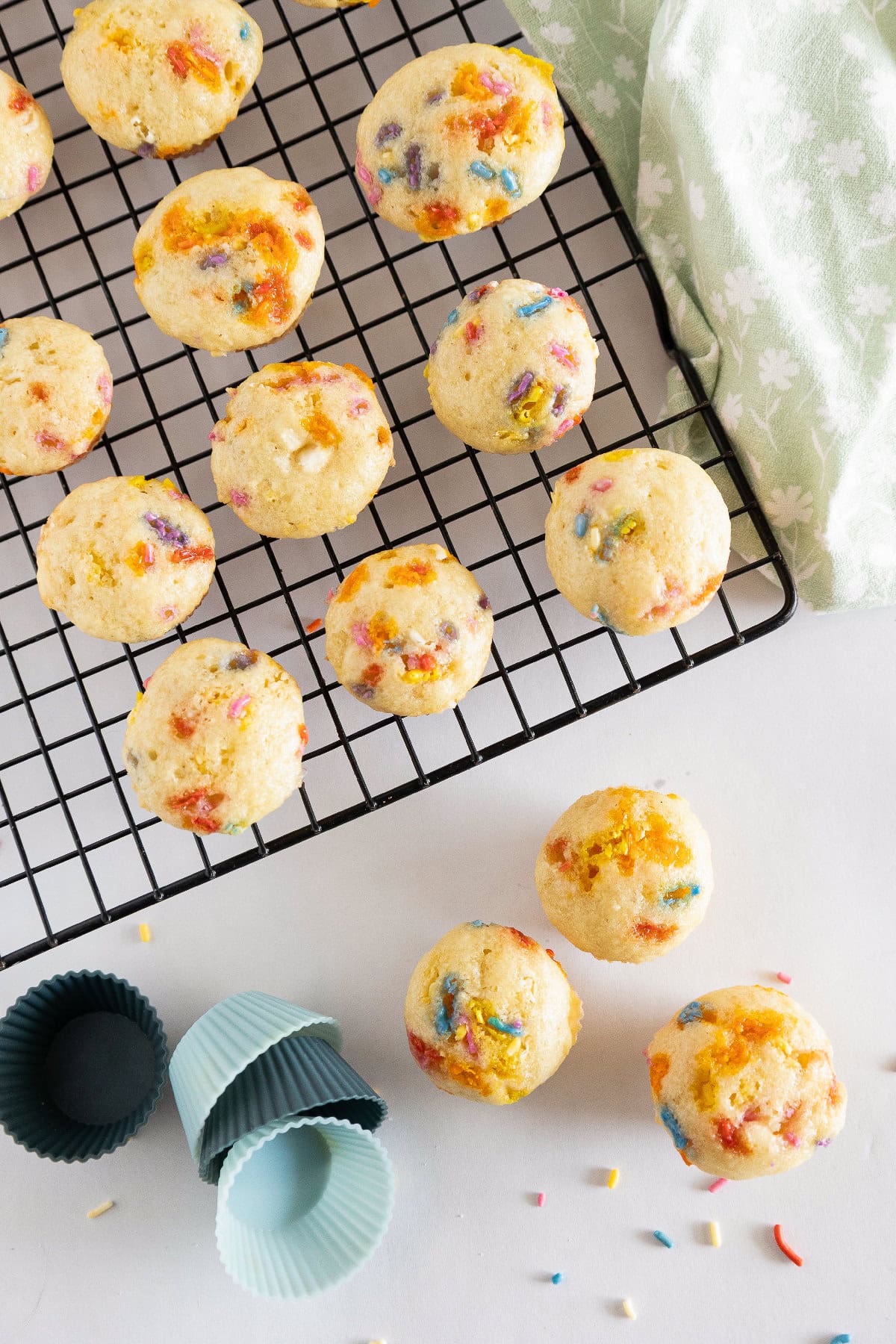 Birthday cake mini muffins on a cooling rack with pastel silicone muffin liners and scattered sprinkles.