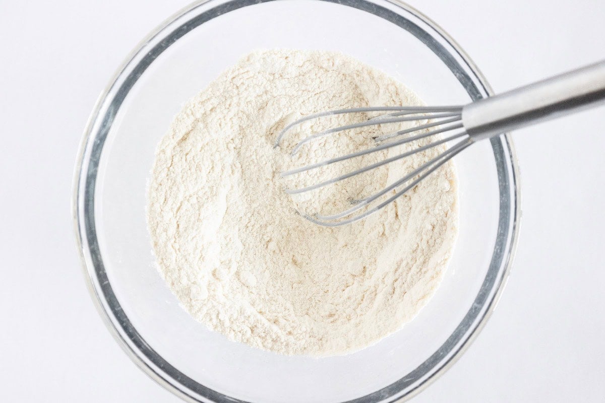 Whisk dry ingredients for birthday cake mini muffins in a glass mixing bowl.