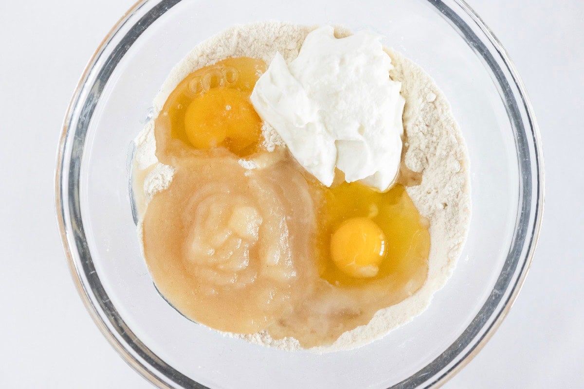 Wet ingredients, including eggs, yogurt, and melted butter, added to dry ingredients for birthday cake mini muffins.