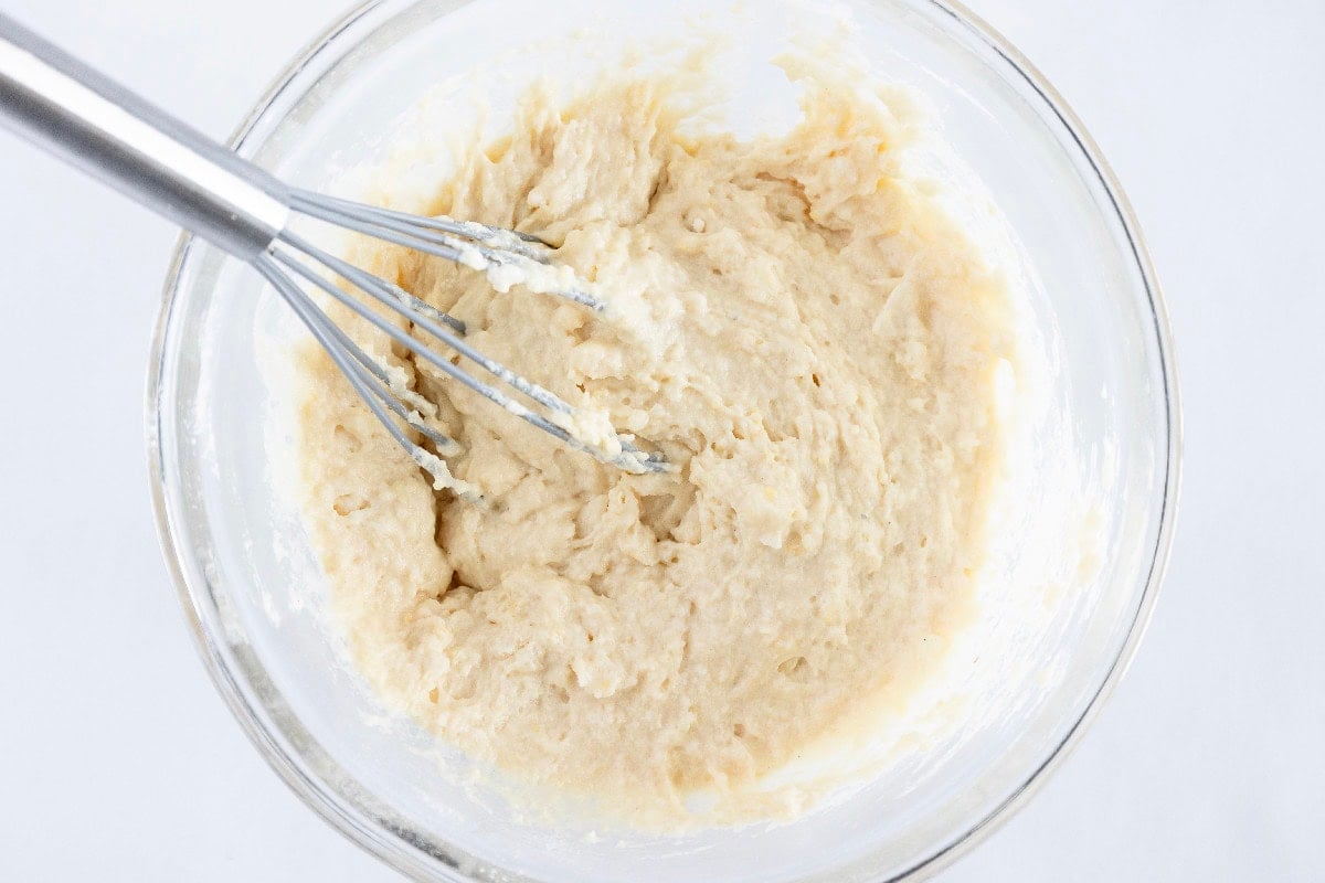 Thick birthday cake mini muffin batter mixed in a glass bowl with a whisk.