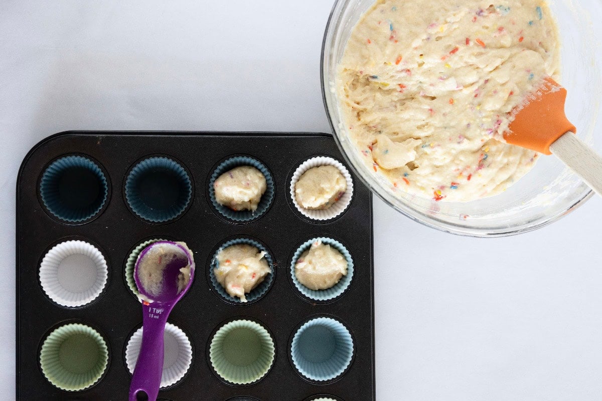 Scooping birthday cake mini muffin batter into silicone-lined mini muffin pan.