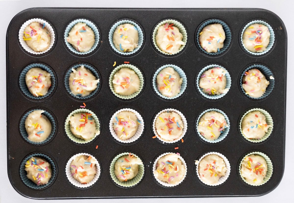 Birthday cake mini muffin batter topped with rainbow sprinkles before baking.