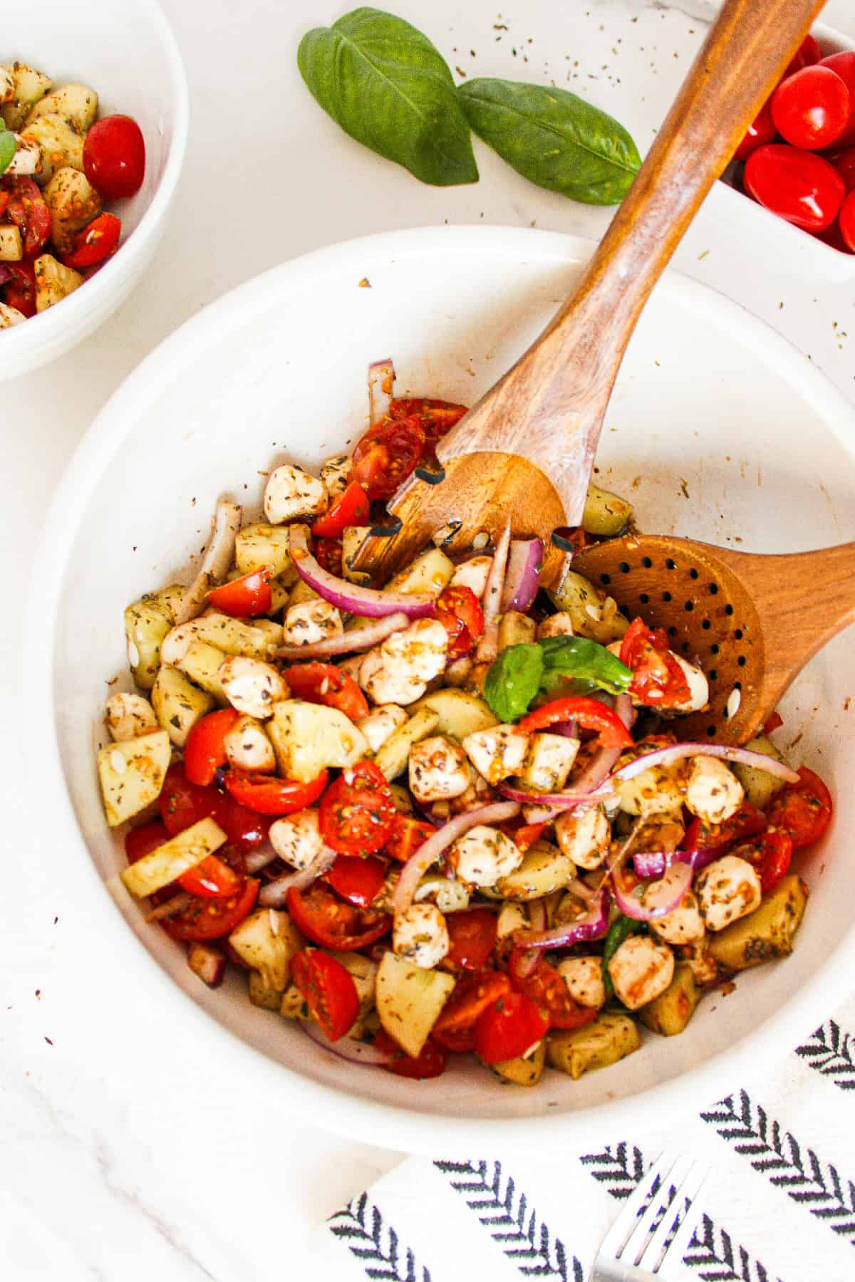 Ingredients for cucumber caprese salad arranged in white bowls, including chopped cucumber, cherry tomatoes, red onion, vegan mozzarella pearls, and dried herbs.
