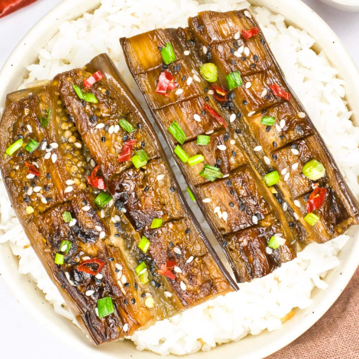 Glazed Japanese-style eggplant scored and served over white rice with sesame seeds, green onions, and red chili slices.