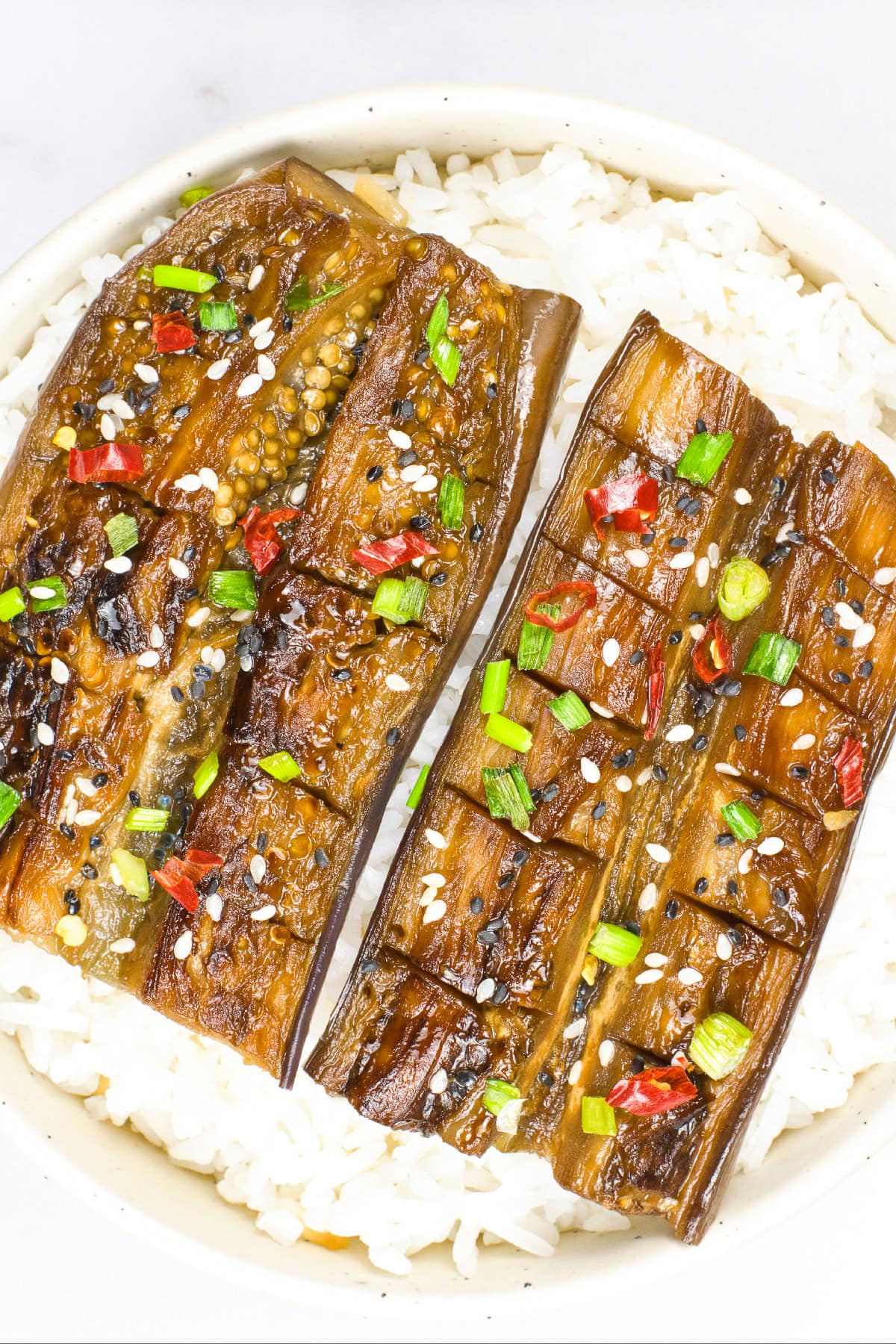 Overhead close-up of vegan unagi-style eggplant glazed in savory sauce and served over steamed white rice with sesame seed garnish.