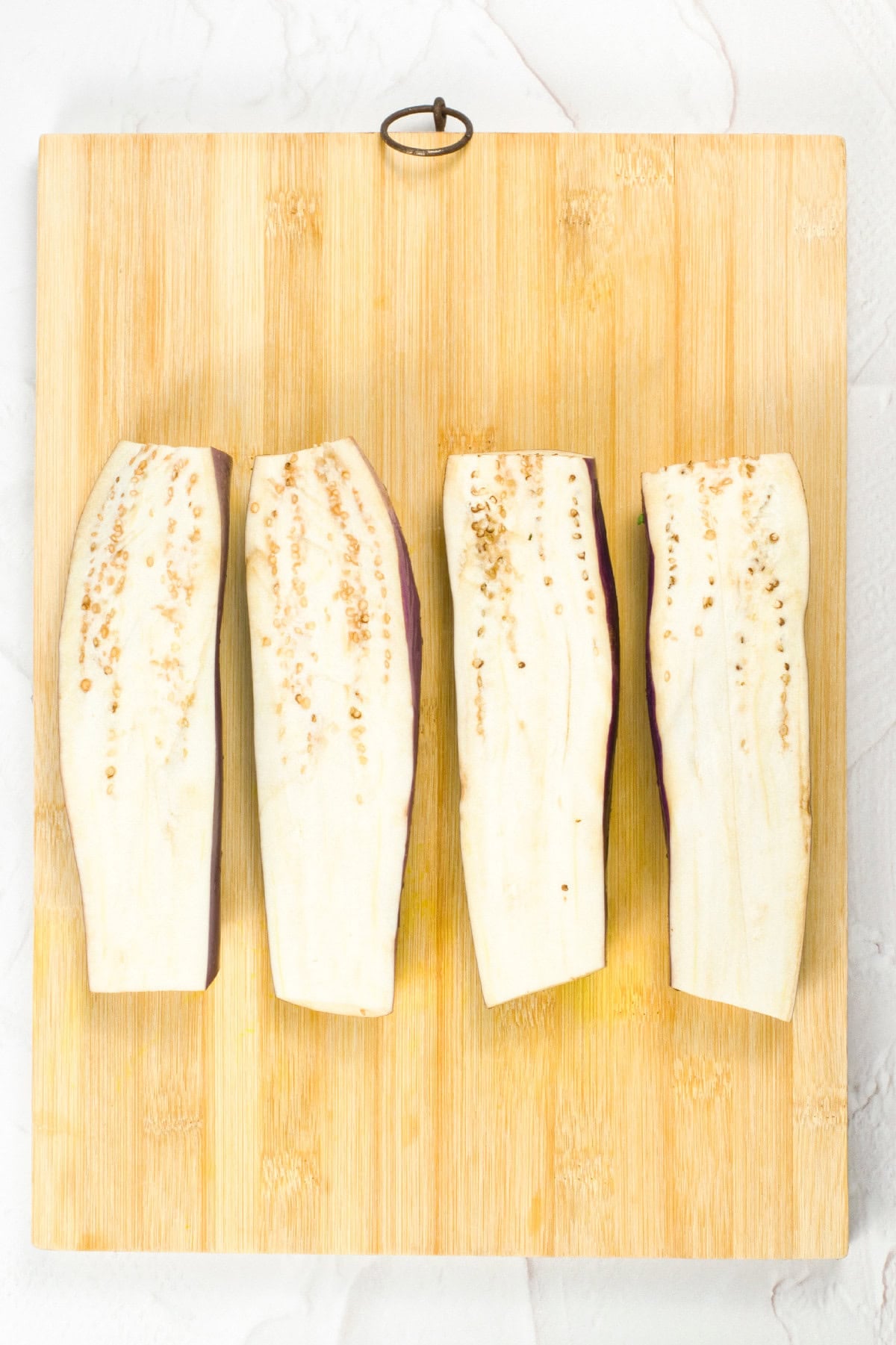 Sliced eggplant halves arranged on a wooden cutting board, prepared for making vegan unagi.