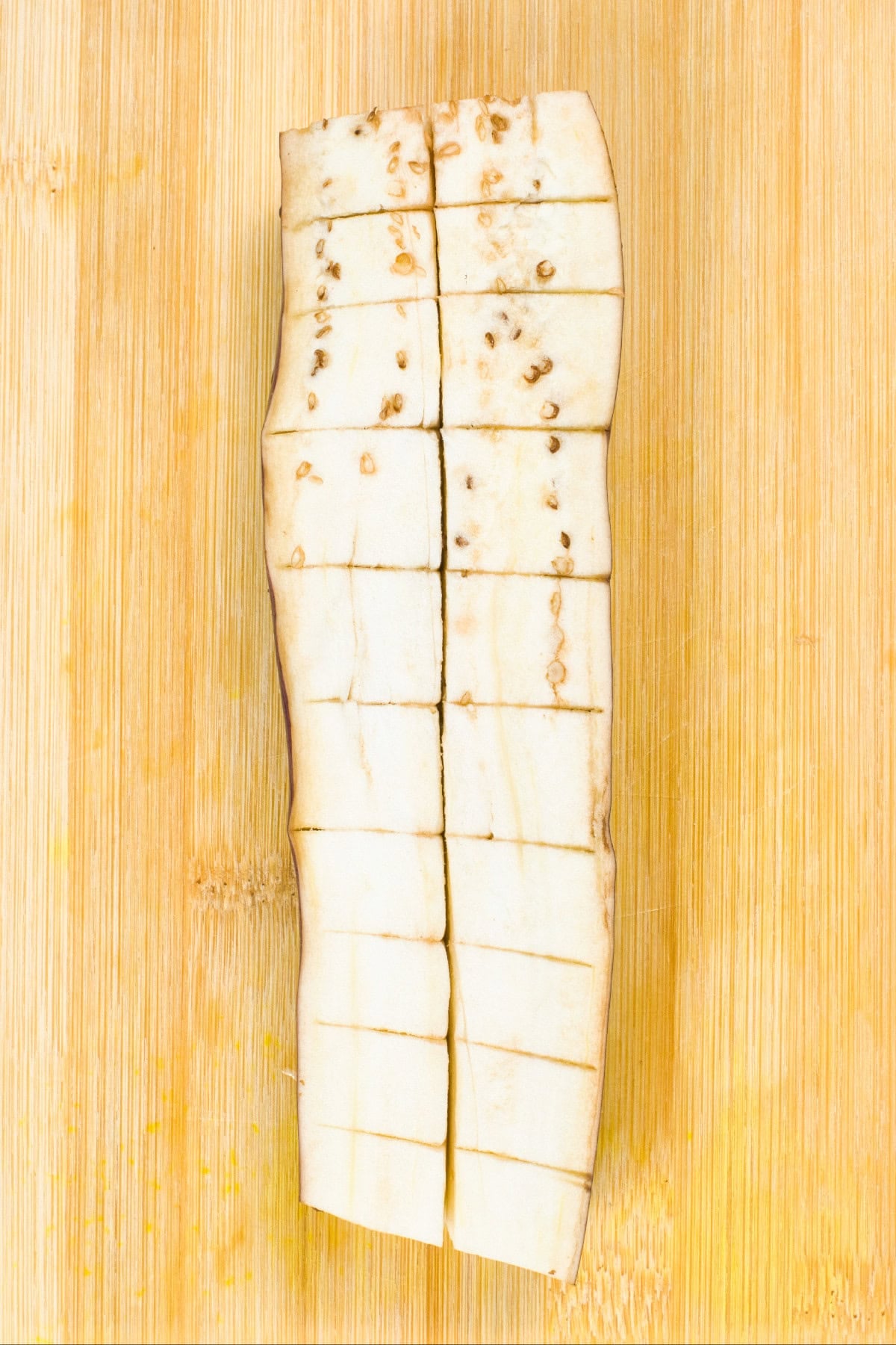 Eggplant half scored in a crosshatch pattern on a wooden cutting board to help absorb sauce and cook evenly.