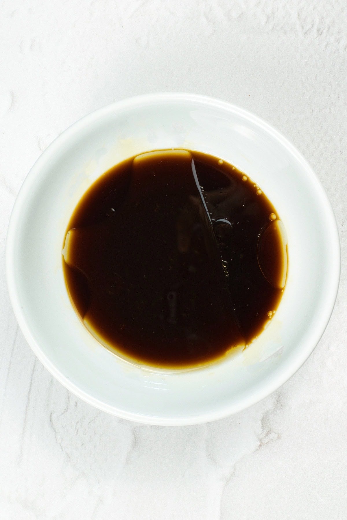 Homemade vegan unagi sauce mixture in a small white bowl on a marble countertop.