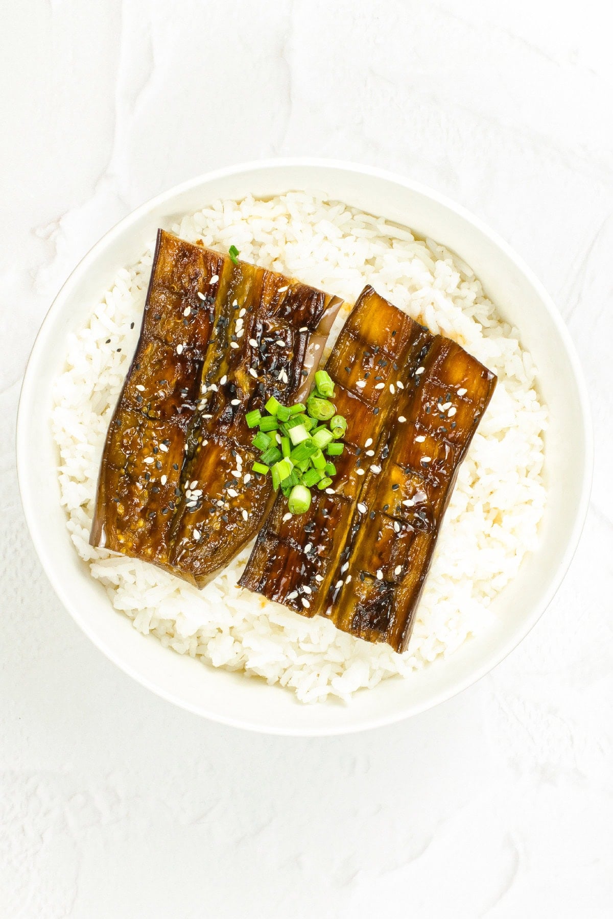 Vegan unagi eggplant bowl topped with chopped green onions and sesame seeds over steamed rice.