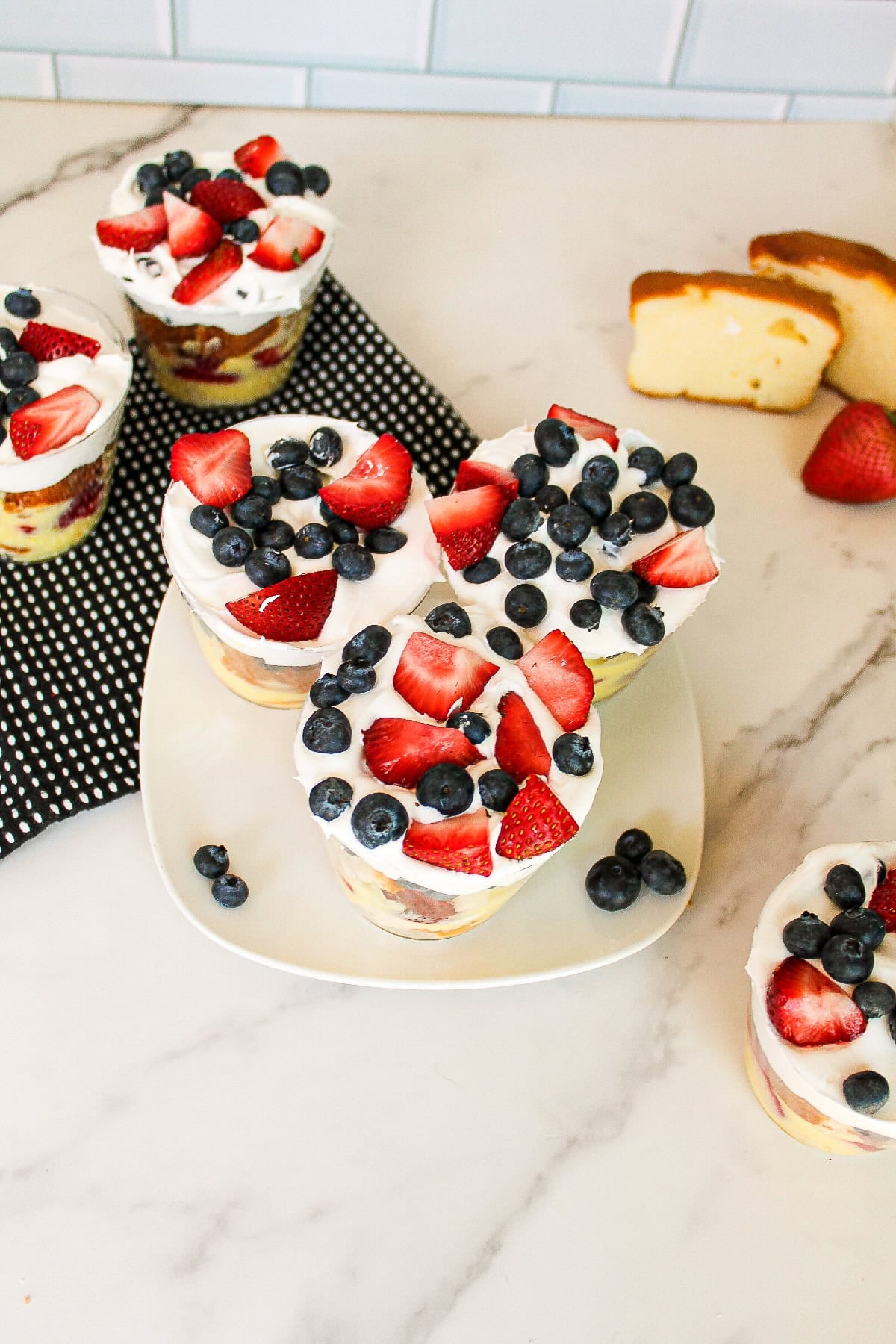 Strawberry and blueberry parfait cups with whipped cream and pound cake served on a marble countertop.