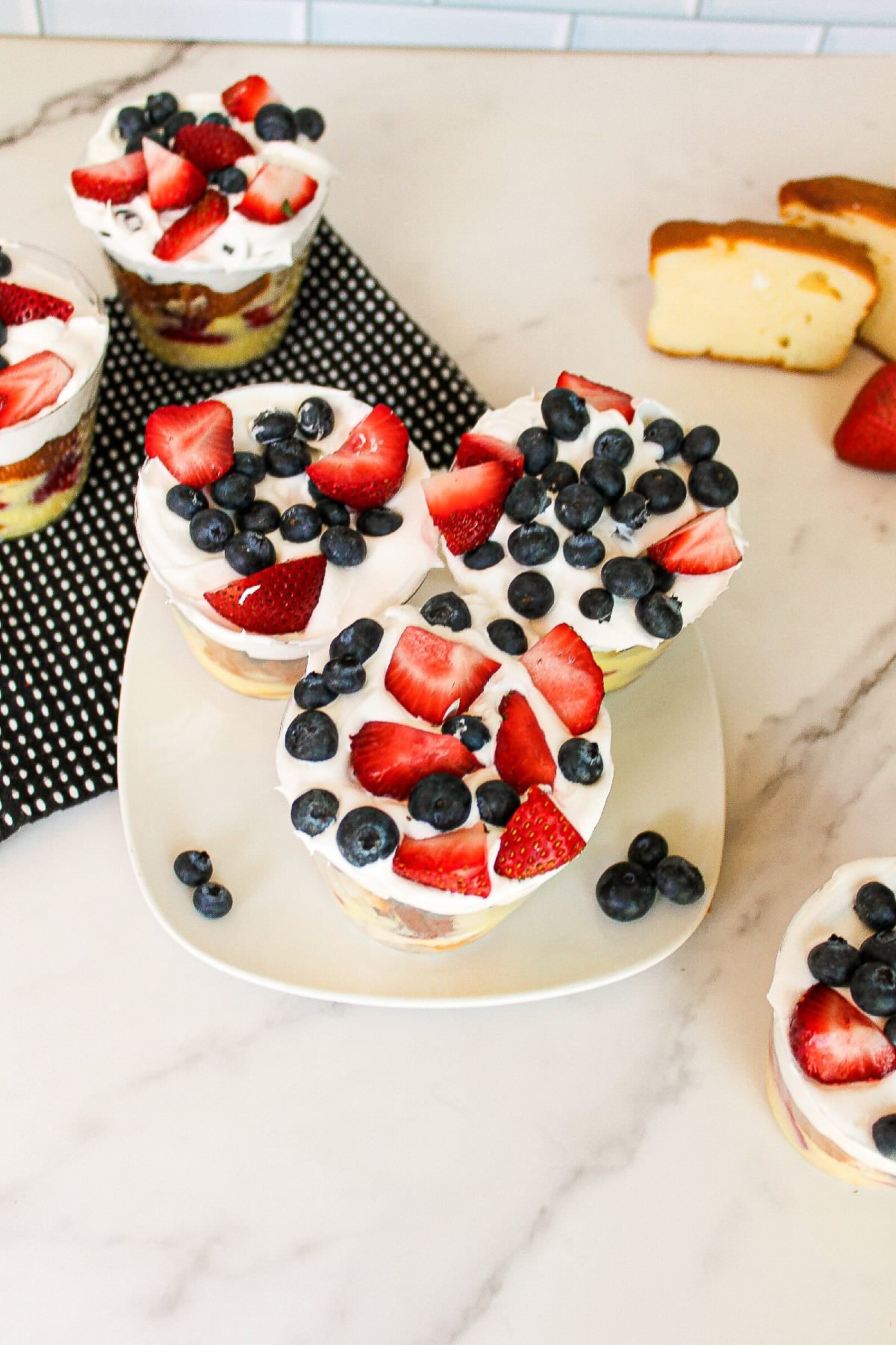 Berry dessert parfait cups layered with vanilla pudding, cake cubes, strawberries, blueberries, and whipped cream.