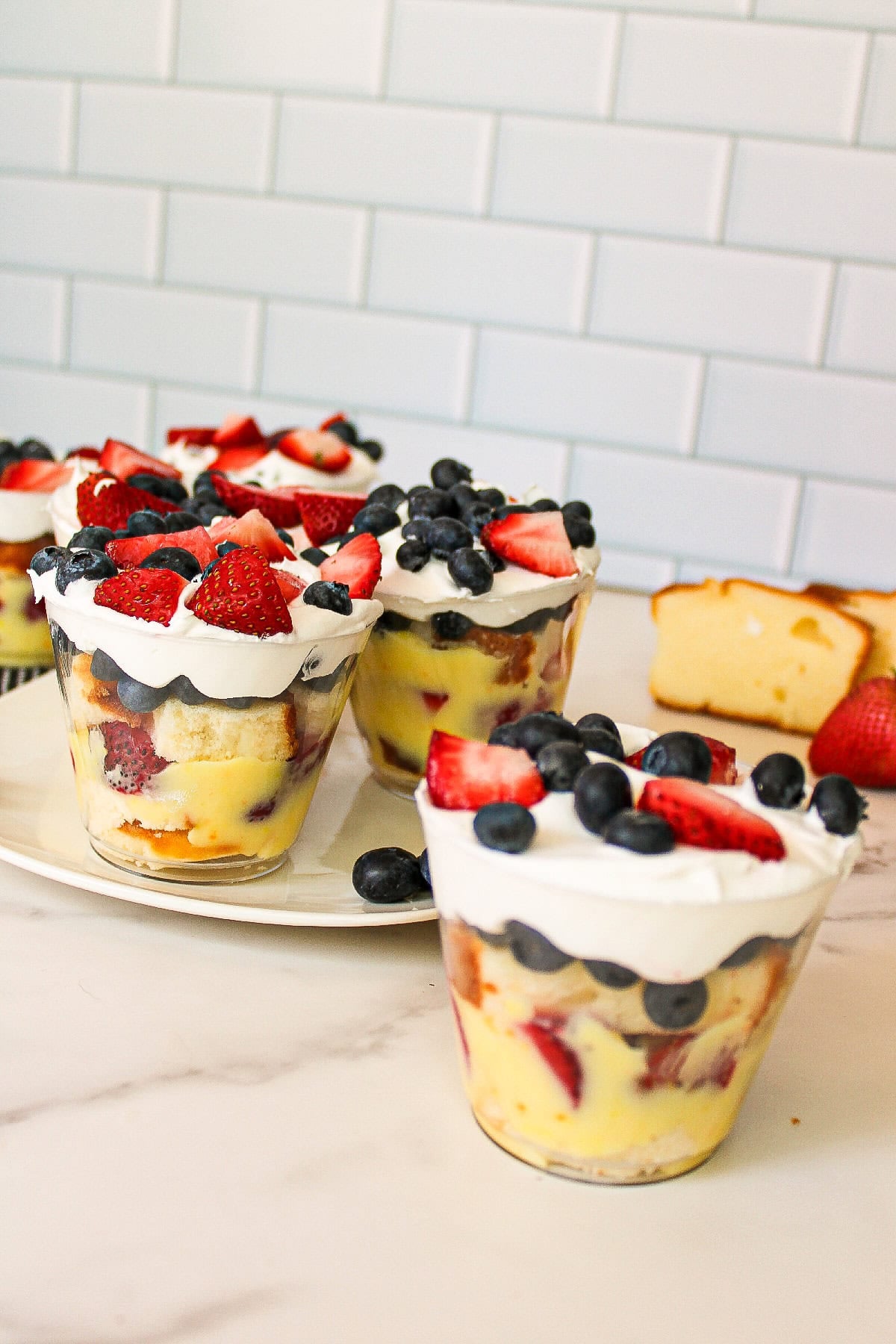 Close-up of layered berry parfait cups with vanilla pudding, whipped cream, strawberries, and blueberries.