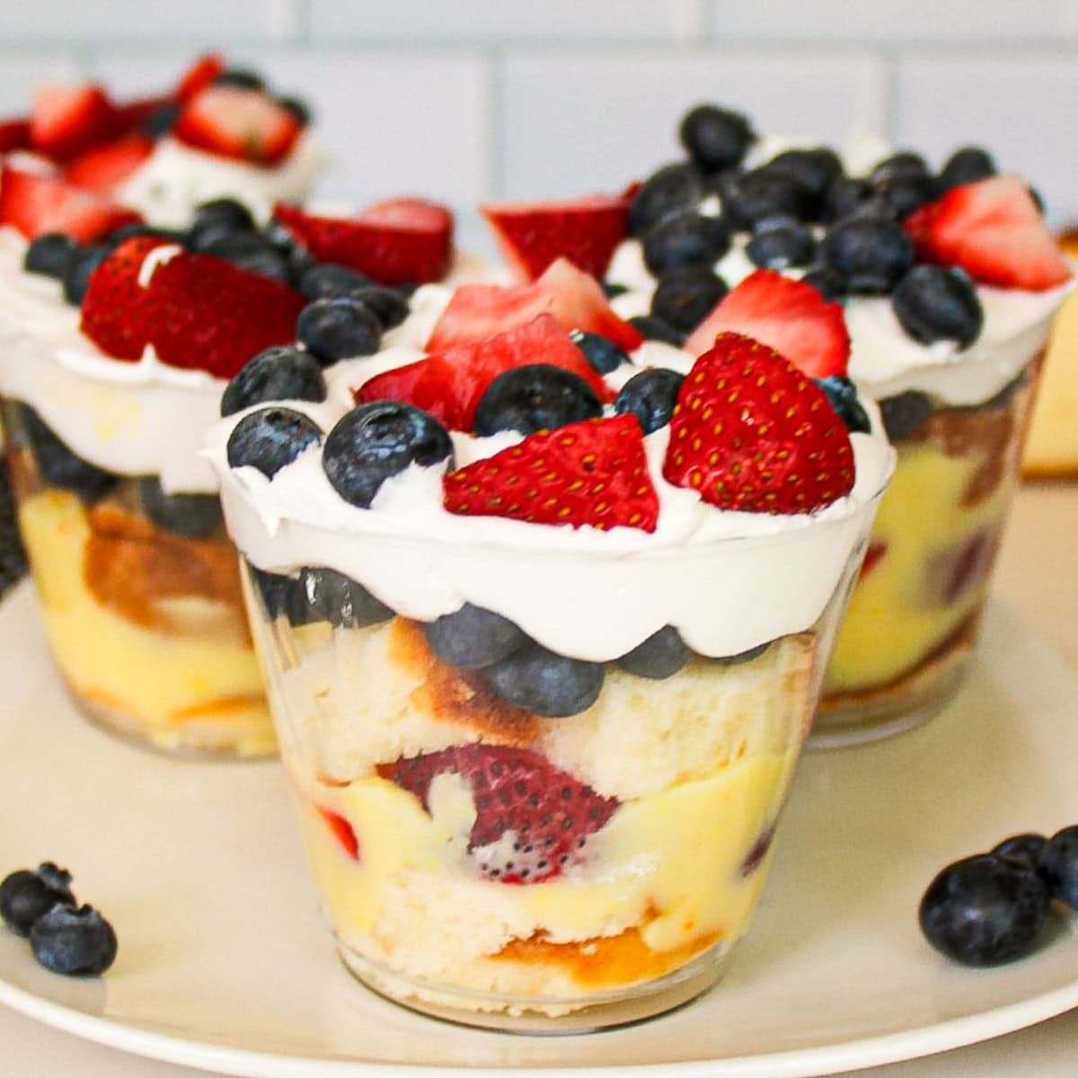 Berry parfait cups layered with vanilla pudding, cake, strawberries, blueberries, and whipped cream.