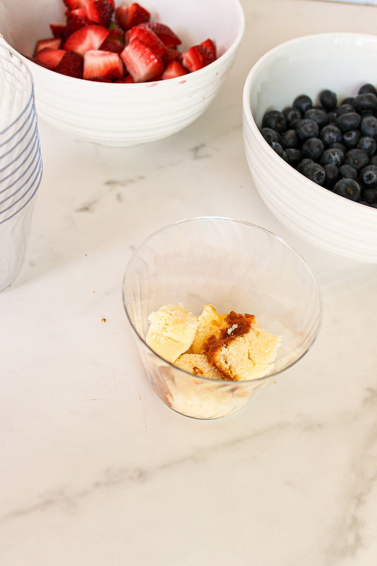 Cubed pound cake layered into a clear plastic parfait cup to begin assembling the dessert.