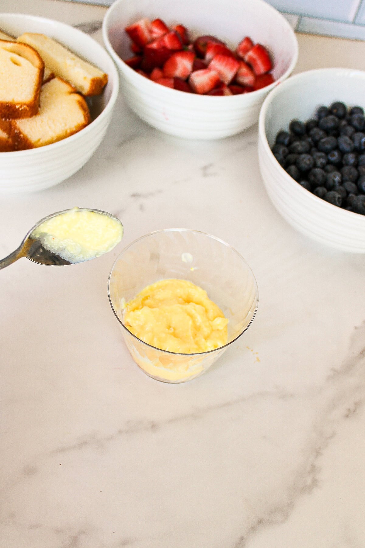 Spoonful of vanilla pudding added over pound cake in a clear parfait cup.