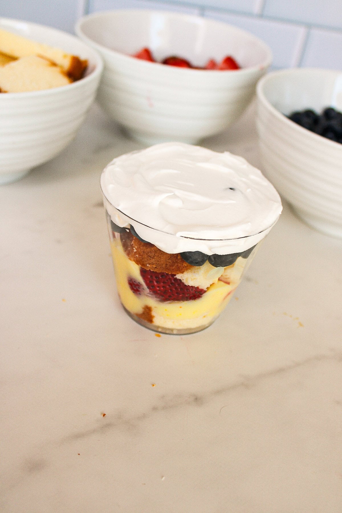 Whipped topping spread over the top of a layered berry parfait cup dessert.